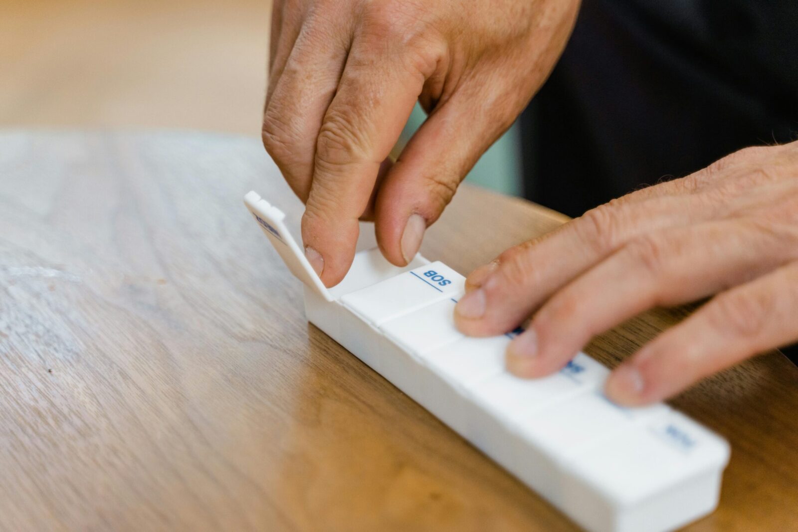 Hands organizing pills in a weekly pillbox, emphasizing healthcare and medication management.